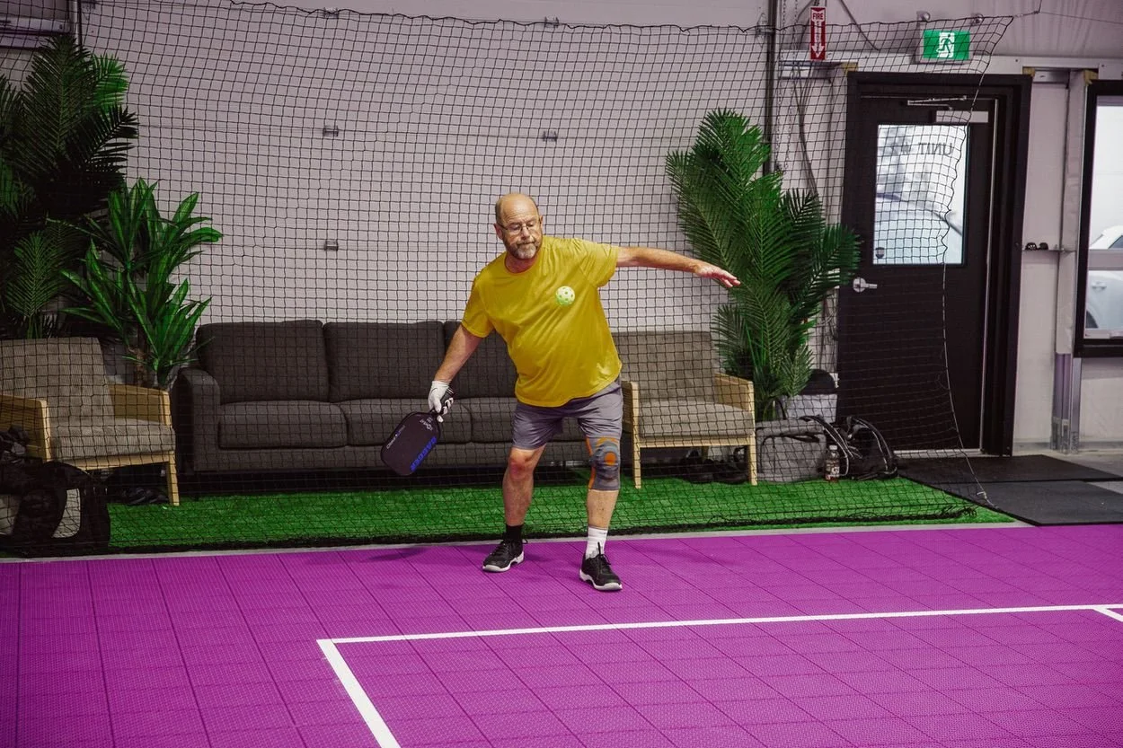 A player hitting a pickleball beside the lounge seating area at Pickleball Cove