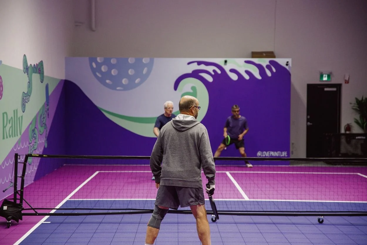Two players rallying on the purple and pink indoor court at Pickleball Cove